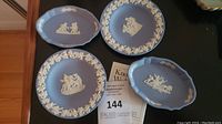Four Wedgwood blue jasperware miniature plates showing classical white low-relief scenes and floral borders