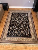 Full view of rectangular rug laid on wood floor showing overall design and fringe ends