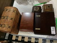 Photo showing five wooden and decorative boxes on tabletop: woven basket style box, two medium wooden boxes, dark wooden box with metal hinges, two small decorative boxes with metal and glass accents
