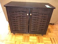 Front view of small dark wood cabinet with two slatted doors featuring a woven lattice design and round metal knobs.