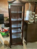 Full view of the dark wooden curio cabinet with glass front and visible shelves, showing the overall structure and style.
