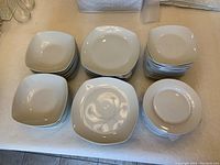 White square plates, bowls, and smaller round bowls stacked on a table.
