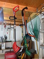 Both red Homelite string trimmer and green Weed Eater edger hanging by their handles in a workshop setting, showing overall condition and storage environment.