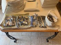 Flatware items displayed on a table with most pieces grouped and bagged by type, along with fabric cases for storage.