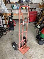 Full side view of the pink metal hand truck showing frame, tires, and loading plate.