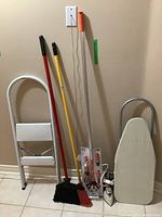 Fold-up step ladder, two brooms, lightbulb changing pole/grip, iron placed next to wall