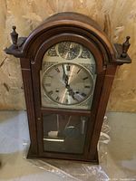 Photo of the wind-up mantle clock showing the full wooden arched case, glass door, and clock face.