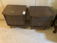 Front view of both nightstands showing two drawers, curved fronts, metal drop handles and tapered legs