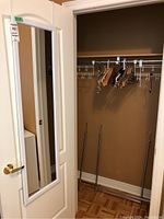 Wall mirror mounted on door and wooden hangers hanging on closet rod taken in a closet with brown walls and parquet flooring.