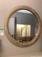 Front view of circular wall mirror mounted on wall, showing the carved bezel as well as reflection of room