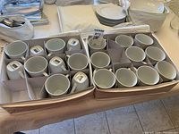 Two boxes containing 24 white coffee mugs arranged neatly in individual compartments.