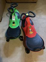Two PlasmaCar ride-on vehicles side by side, green and red, showing full bodies and steering wheels.