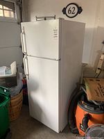 Front view of white GE top-freezer refrigerator in garage.
