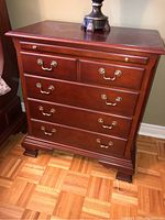Front view of nightstand showing five drawers with brass pull handles and small upper knobs, light wood grain visible, minor surface wear on drawer fronts.