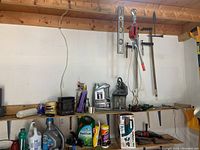 Shelf with various automotive oils, cleaning and garden products including Mobil 1 motor oil, Armor All cleaner, and Weed & Gon weed killer. Tools and hoist hanging on wall above shelf with a black lantern.