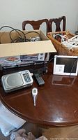 Overview photo of assorted electronics on table, showing radio, thermometer, senior day/time display and baskets with extension cords.