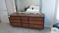 Full view of large solid wood dresser with nine drawers and mirror resting on top.