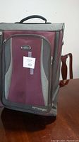 Front view of burgundy and gray suitcase showing front zippered pocket and top handle with MaxSold lot tag 40 attached.
