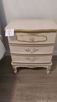 Front view of vintage style night stand showing three drawers and ornamental gold accents