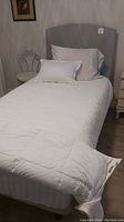 Complete single bed set up with white quilted bedding and pillow, gray upholstered headboard visible