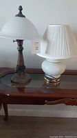 Two small table lamps on a glass-top wooden table, showing the different base styles and lamp shades.