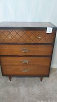 Front view of tall wooden dresser showing diamond pattern on top drawer and metal handles on lower drawers