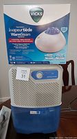 Vicks Warm Steam Vapourizer in box and Simplicity dehumidifier side by side from front view showing general condition and packaging.