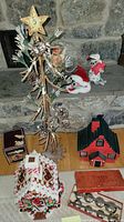 Metal Christmas tree with star topper, two snowman Annalee figurines, red and black ceramic cabin house, white ceramic gingerbread-style house, boxed Giles Bells musical bells, orange Giles Bells box on floor and stone hearth.
