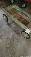 Full view of antique metal wagon showing rusted painted metal bed and wheels on concrete floor