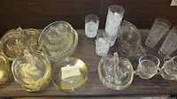 Full lot overview of glass apple-shaped plates, leaf-shaped tray, glassware, coffee cups, and round gold-rimmed plate on table