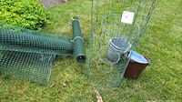 Green plastic-coated wire fencing rolls and metal tomato cages with garden pots on grass.