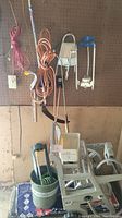 Photo showing hanging pink and orange garden hoses, blue hose reel, and garden cart with bucket on floor