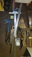 Shop supplies including saw, rulers, broom, staple gun, rope, mallet, and other tools hanging on peg wall.