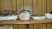 Shelf with multiple CorningWare baking and serving dishes with blue flower pattern and metal trivets