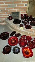 Overview of red glass serving and decorative pieces arranged on a raised brick hearth and floor