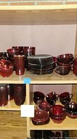 Shelves with assorted red/ruby depression glass bowls, plates, and cups arranged and grouped by type and size.