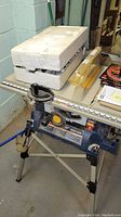 Blue Ryobi 10-inch table saw on foldable metal stand, with white foam packaging on top.