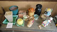 Lot of 13 ceramic vases, planters, and decorative figures displayed on a wooden surface, showing assortment and condition.
