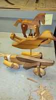 Photo of three vintage wooden toys on a workbench: a rocking horse, a duck on stand, and a wooden airplane with propeller and wheels.