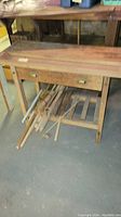 Front view of wood work table with drawer and wooden pieces stored underneath, showing wear and natural wood finish.