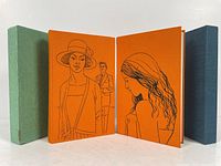 Two hardcover books with illustrated orange covers and protective slipcases, showing front and back covers with line art of characters.