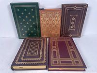 Five leather bound books arranged standing and stacked to show front covers and spines with embossed gold designs.