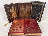 Front view of the five leather-bound books showing ornate gold embossed covers of various colors and designs.