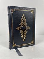 Front cover of the book showing black leather with ornate gold detailing.