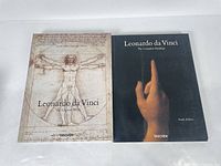Two hardcover books front-facing: one with Vitruvian Man cover, one with hand pointing upwards cover by Taschen.