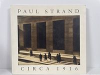Front cover of the Paul Strand Circa 1916 photography book showing the title and a sepia photo of people near large building windows.