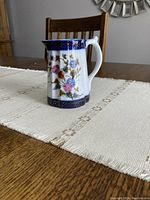 Side view of small porcelain hand painted creamer with floral patterns and cobalt blue and gold decorative trims on table.