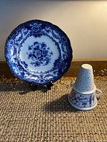 Full view of flow blue floral plate and cone-shaped Meissen jelly strainer placed on woven mat