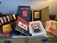Chinese proverbs book, Korean tribal masks, brocade art, paper cuts of Chinese opera facial makeup, two doll costumes displayed together.
