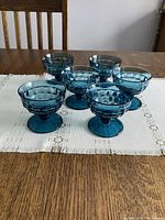 Front view of six teal blue glass dessert dishes arranged on a table showing textured honeycomb pattern and rounded bases.